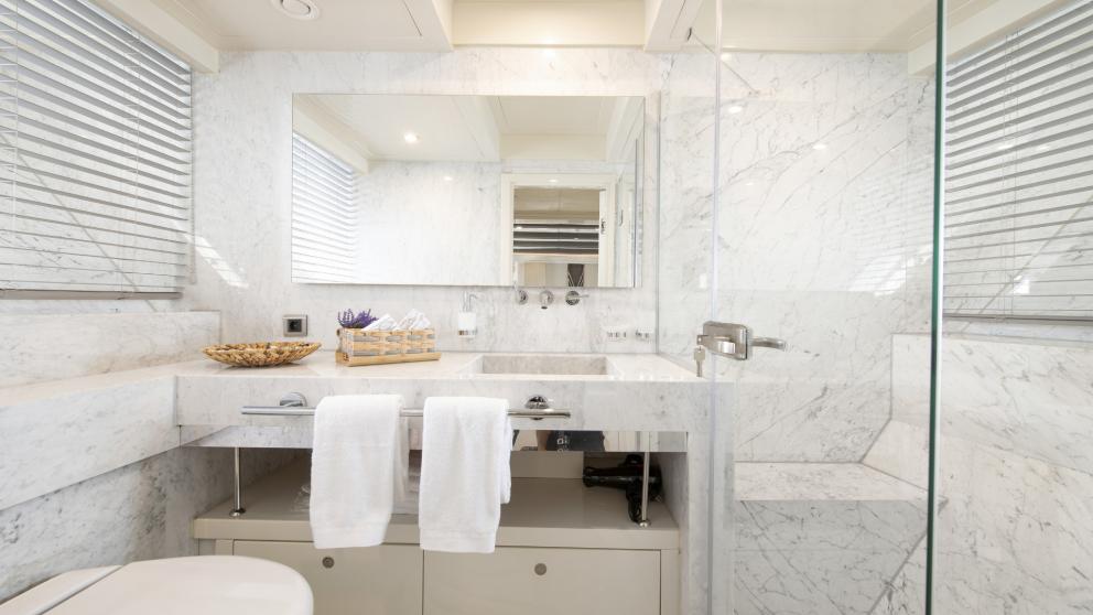 A marble-clad bathroom with shower, washbasin, toilet and simple decoration.